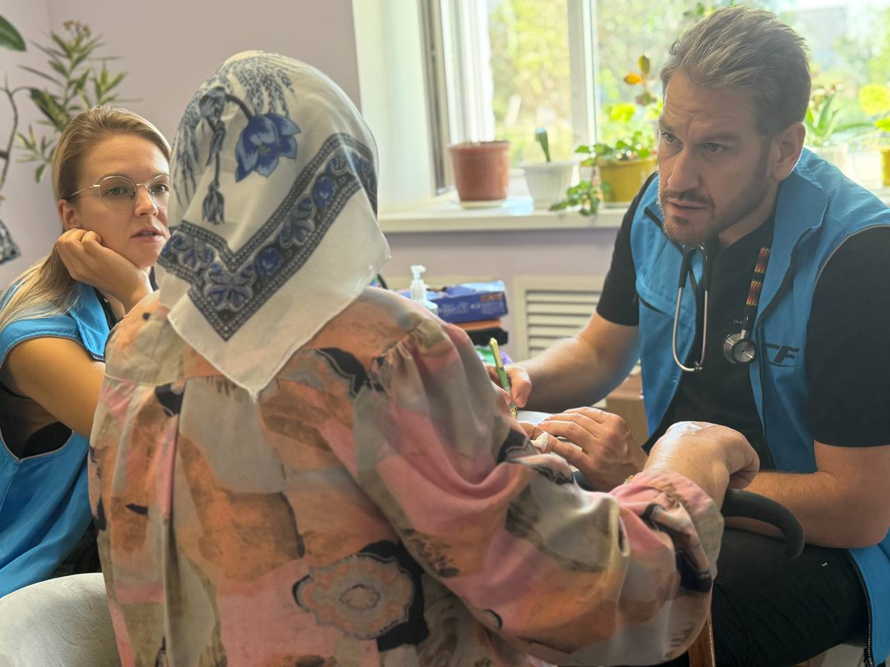 Two GCF medical volunteers in blue field vests care for an older woman.