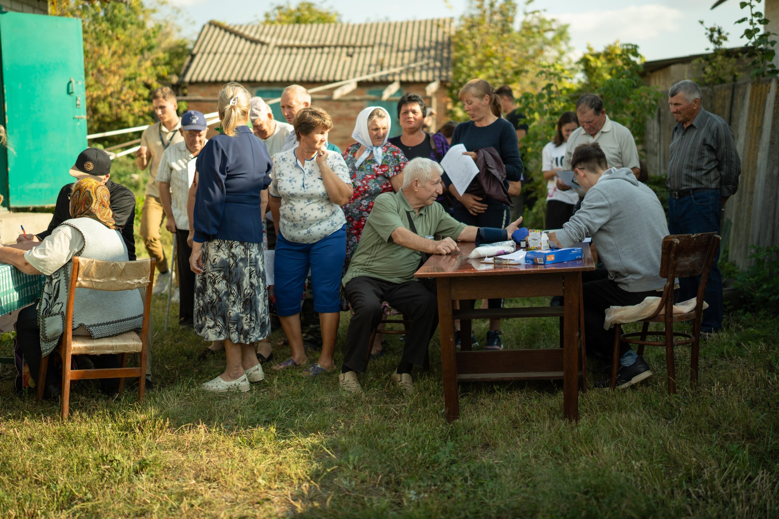 Patients and volunteers gather around an outdoor clinic in a Ukrainian village.