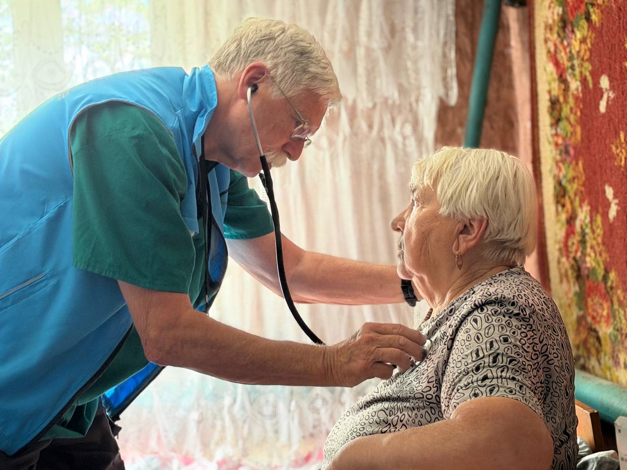 A GCF clinician examines a seated patient with a stethoscope.